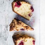 Four wedges of raspberry streusel coffee cake on a white wooden background.