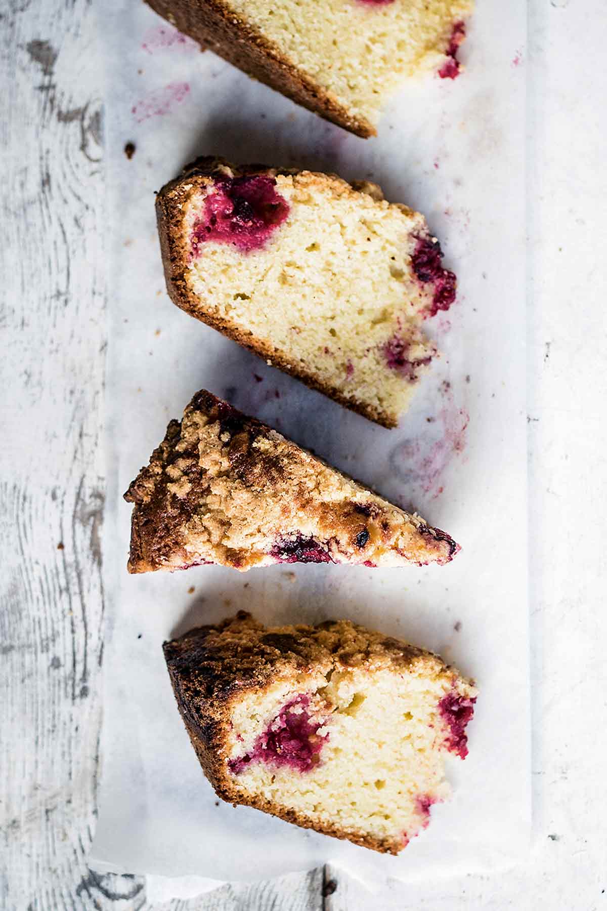 Four wedges of raspberry streusel coffee cake on a white wooden background.