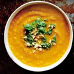 A bowl of roasted carrot soup with cilantro and mint relish and peanuts on top.