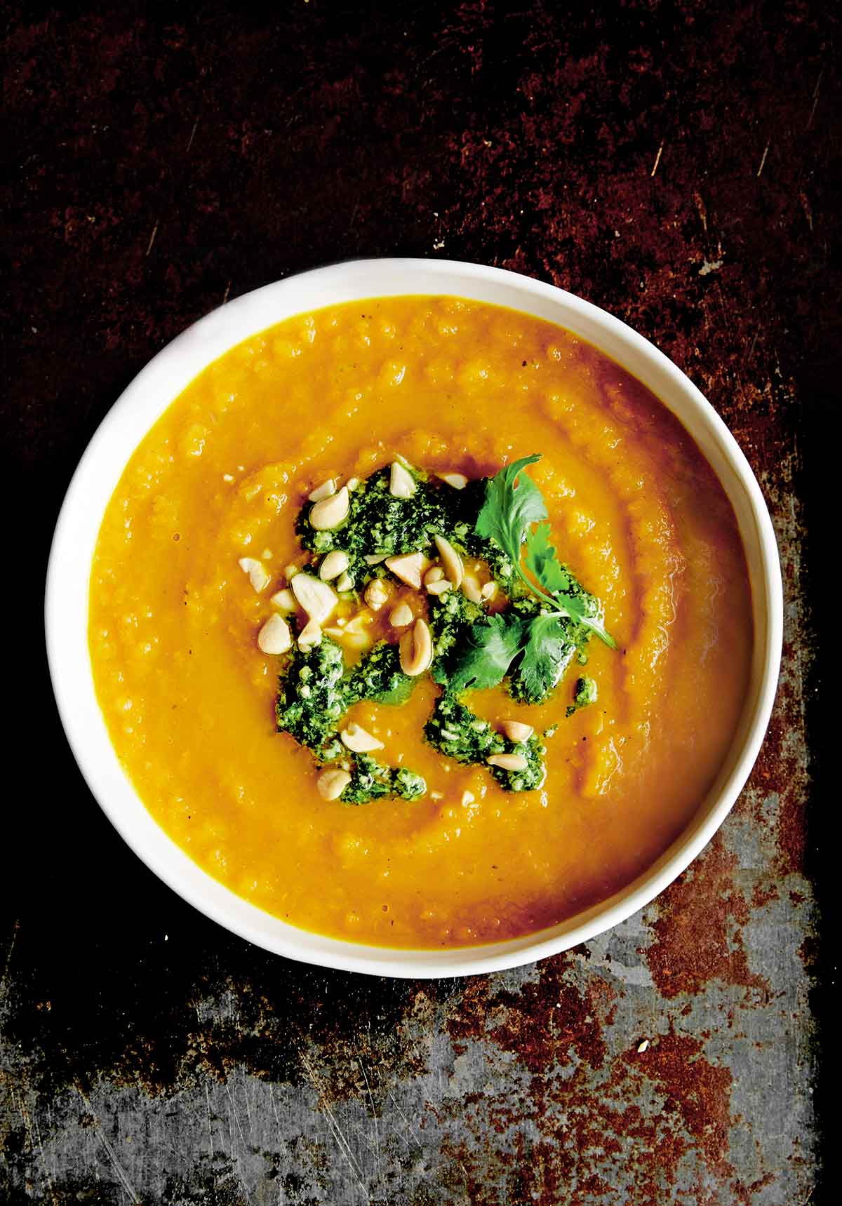 A bowl of roasted carrot soup with cilantro and mint relish and peanuts on top.