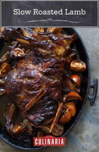 A slow roasted lamb shoulder in an oval cast iron dish with orange wedges.