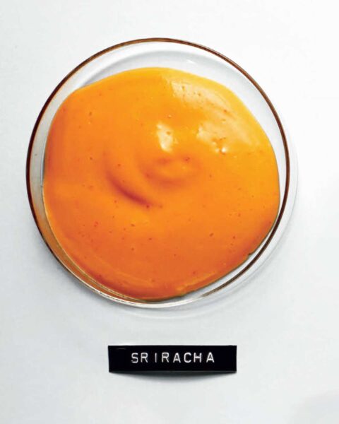 A glass bowl filled with Sriracha mayonnaise and a typed label underneath.