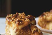 A sticky bun topped with caramel and pecans on a plate, with more sticky buns in the background.