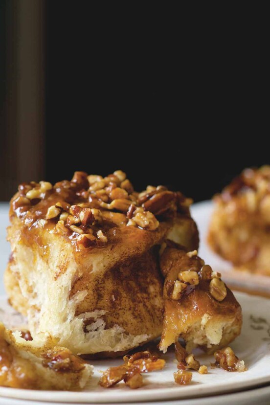 A sticky bun topped with caramel and pecans on a plate, with more sticky buns in the background.