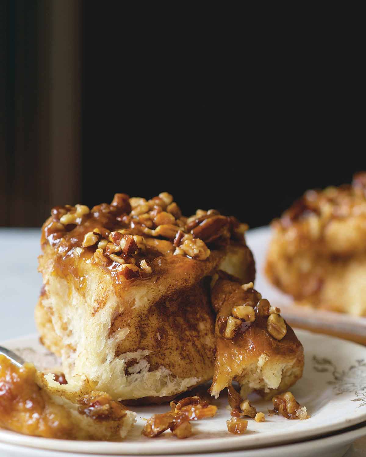 A sticky bun topped with caramel and pecans on a plate, with more sticky buns in the background.