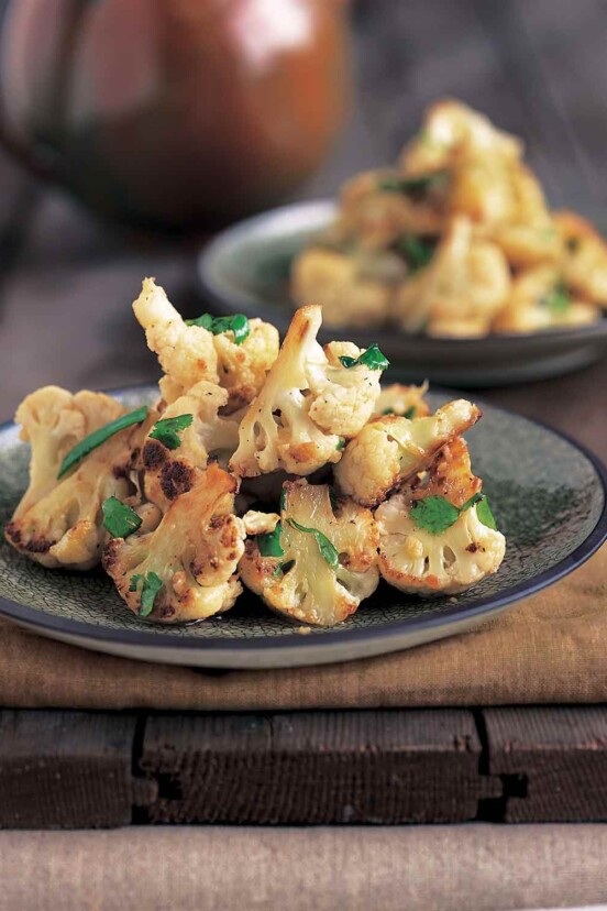 Two grey plates topped with stir-fried cauliflower, and garnished with fresh cilantro on a wooden board.