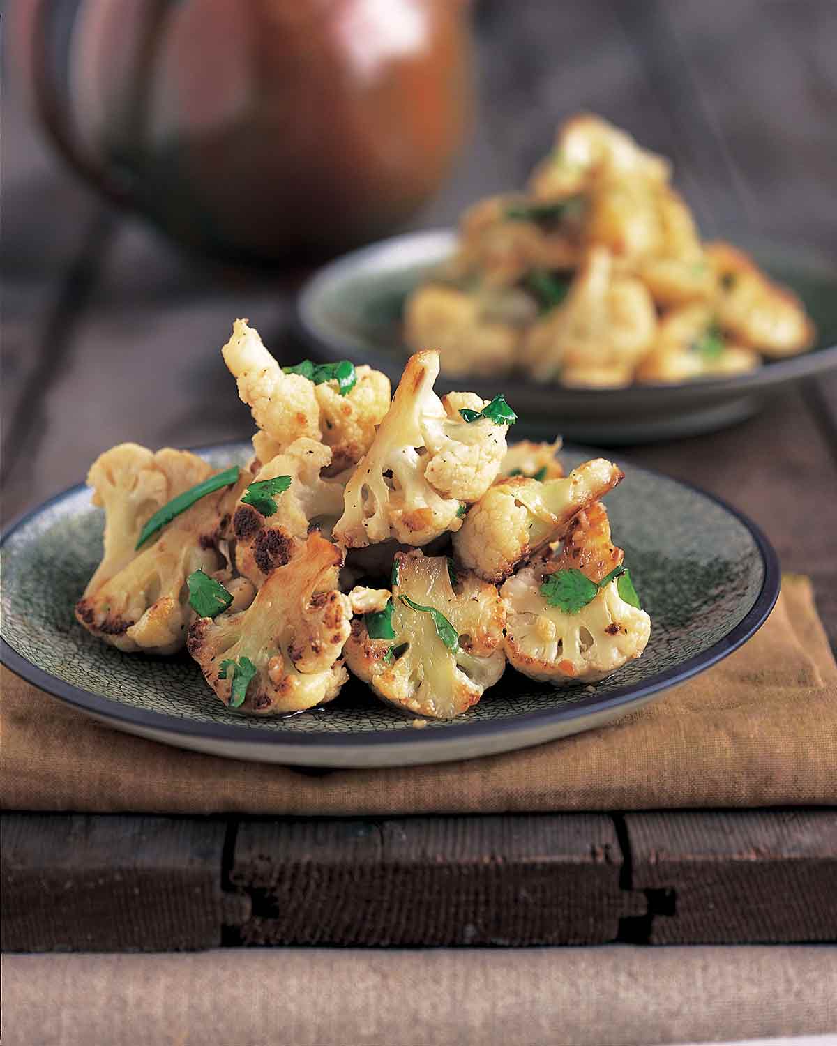 Two grey plates topped with stir-fried cauliflower, and garnished with fresh cilantro on a wooden board.