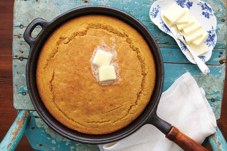 A cast-iron skillet filled with a cooked sweet potato cornbread with two pats of butter on top and a dish of butter pats beside it.