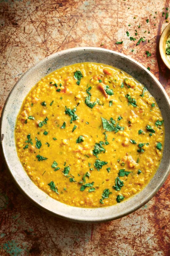 A ceramic bowl filled with tarka dal and sprinkled with cilantro with a small bowl of chopped cilantro on the side.