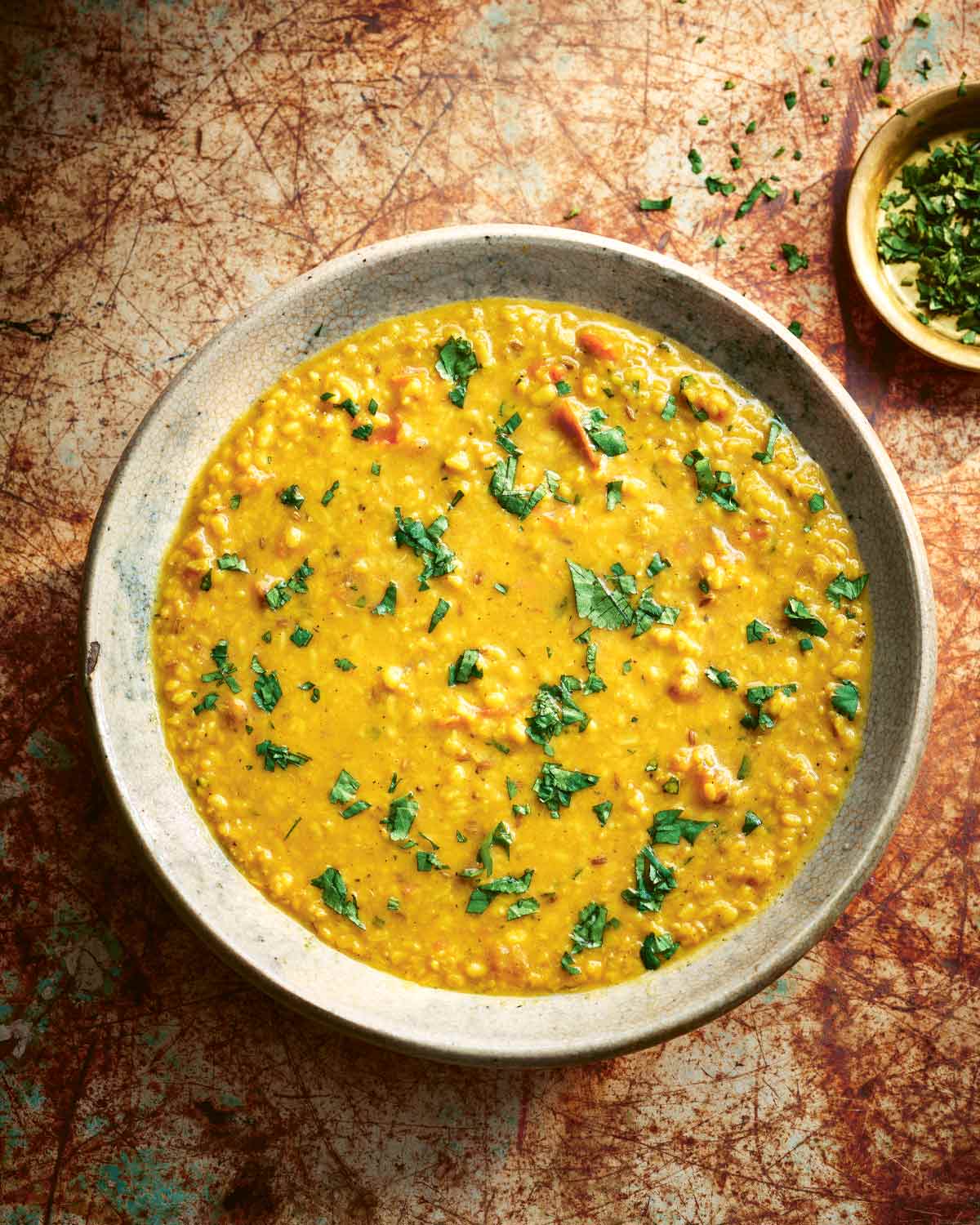 A ceramic bowl filled with tarka dal and sprinkled with cilantro with a small bowl of chopped cilantro on the side.