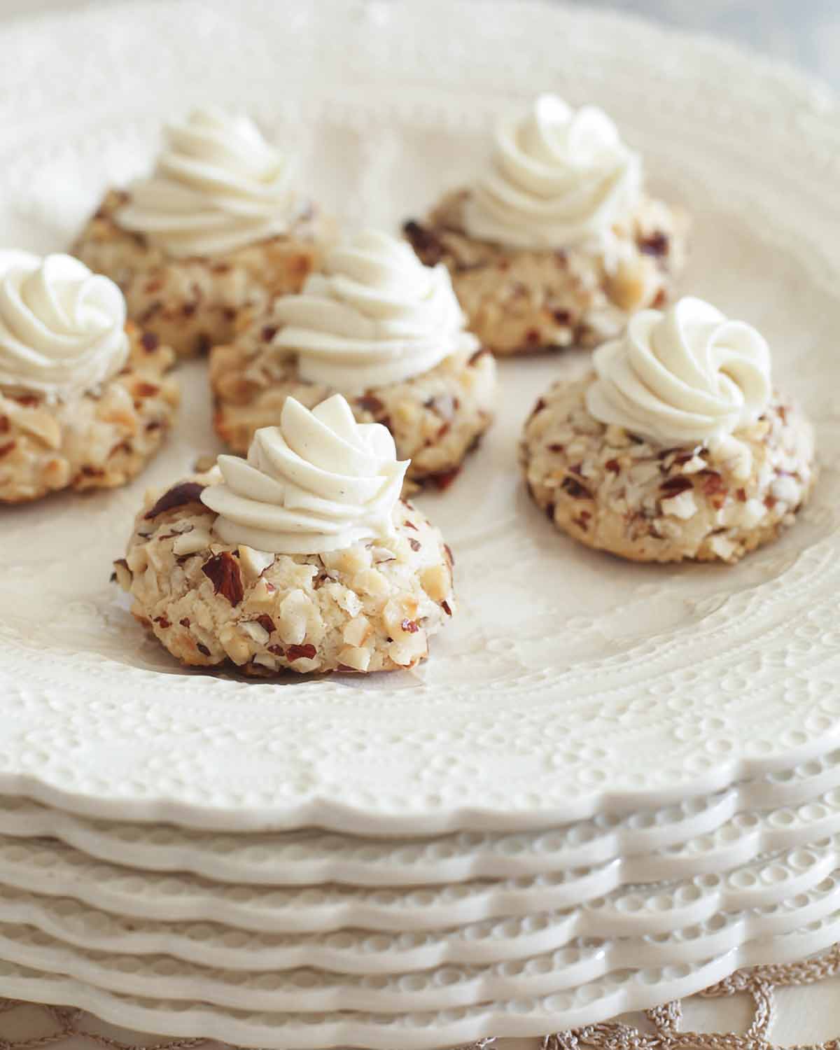 A stack of scalloped white plates with six thumbprint cookies on top, each garnished with white chocolate ganache.