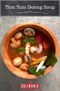 A wooden bowl filled with tom yum goong soup with mushrooms, lemongrass, shrimp, and cilantro in a broth.