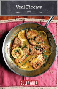 Four veal cutlets in a white wine lemon sauce with lemon slices and capers in a skillet for veal piccata.
