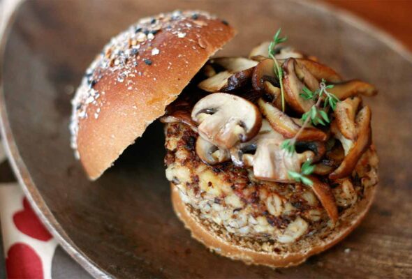 A veggie burger topped with mushrooms and thyme on an oval plate.