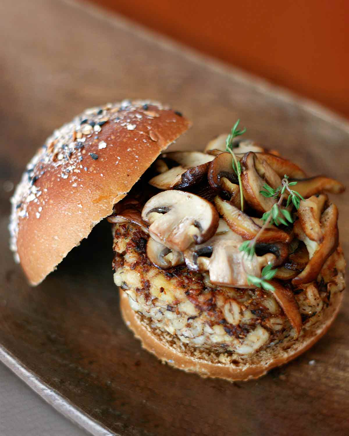 A veggie burger topped with mushrooms and thyme on an oval plate.