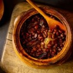 A pot of Appalachian cider baked beans with a wooden spoon placed on a wooden chair.