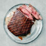 An Asian grilled flank steak, with several medium rare sliced cut from it, the outside crisscrossed with grill marks--on a plate