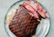 An Asian grilled flank steak, with several medium rare sliced cut from it, the outside crisscrossed with grill marks--on a plate