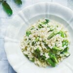 A plate and a bowl of asparagus risotto with a fork resting beside the bowl.