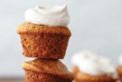 Three banana bread muffins stacked on top of each other with chai whipped cream on top and more muffins on a plate in the background.