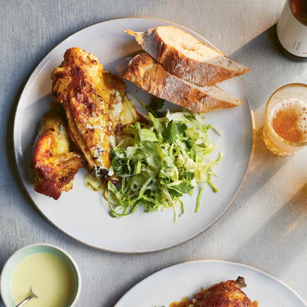Two plates of beer-brined bbq chicken, shredded cabbage, and artisan bread, with a small bowl of dip between them.