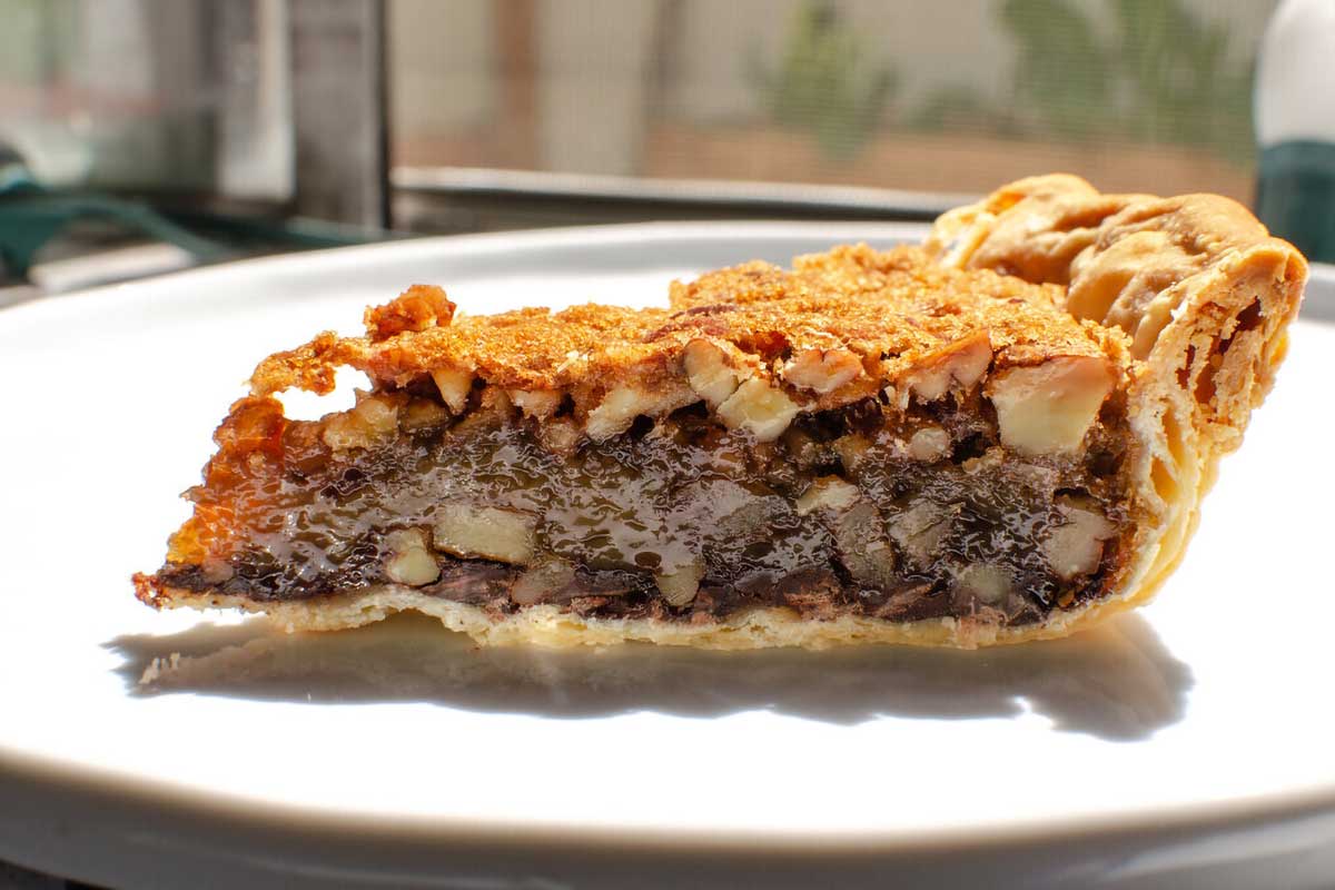 A side view of a slice of black bottom pecan pie.
