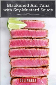 Slices of blackened ahi tuna with soy-mustard sauce lined up next to each other with two lime wedges on the side.