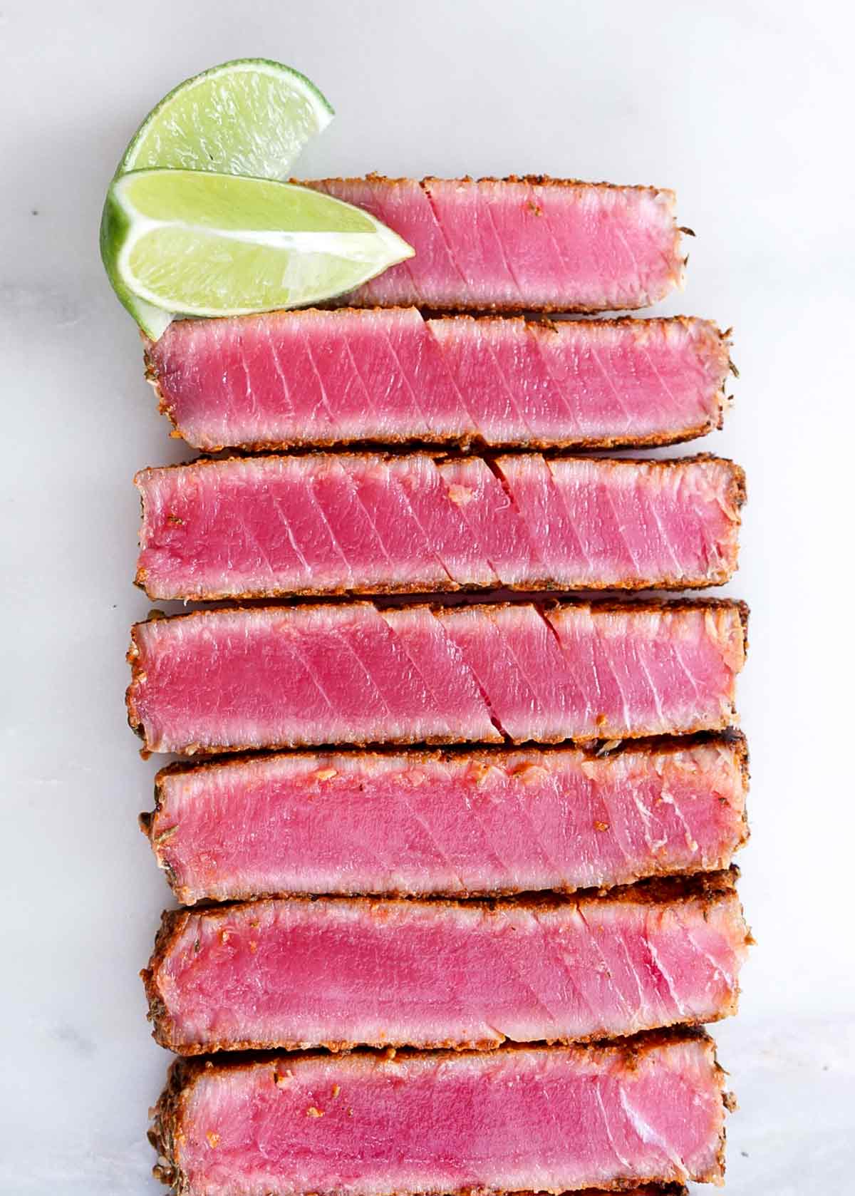 Slices of blackened ahi tuna with soy-mustard sauce lined up next to each other with two lime wedges on the side.