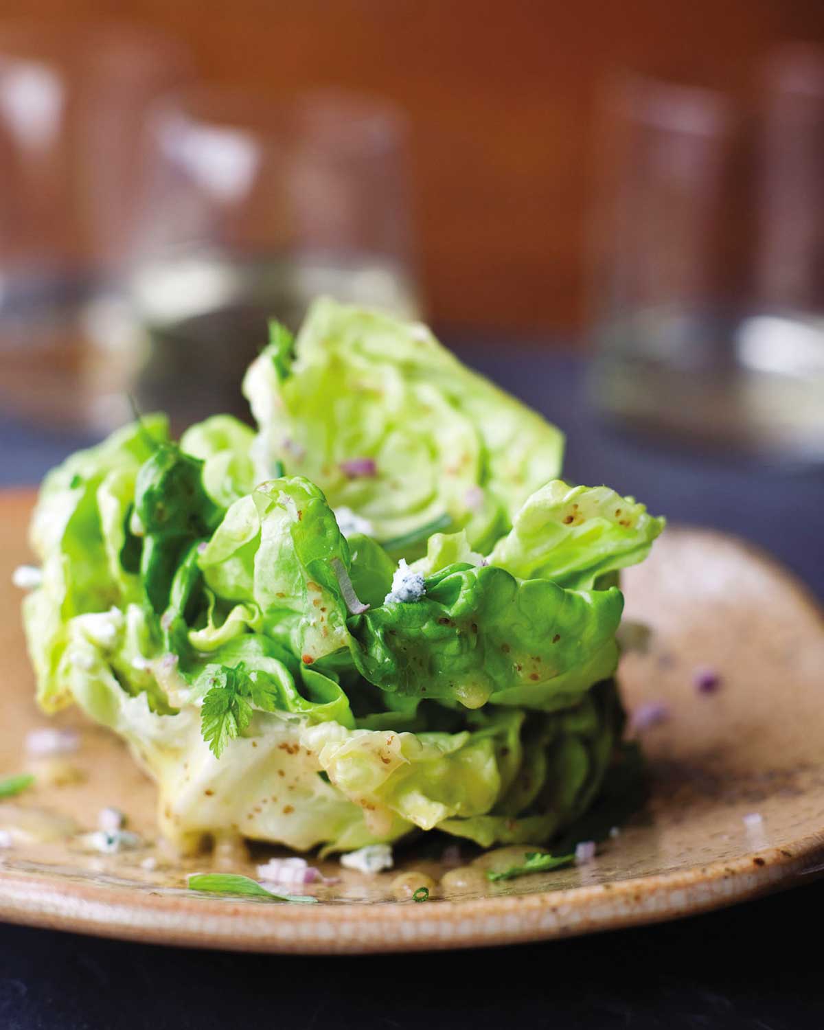 A salad of butter lettuce with maytag blue cheese on a brown plate.