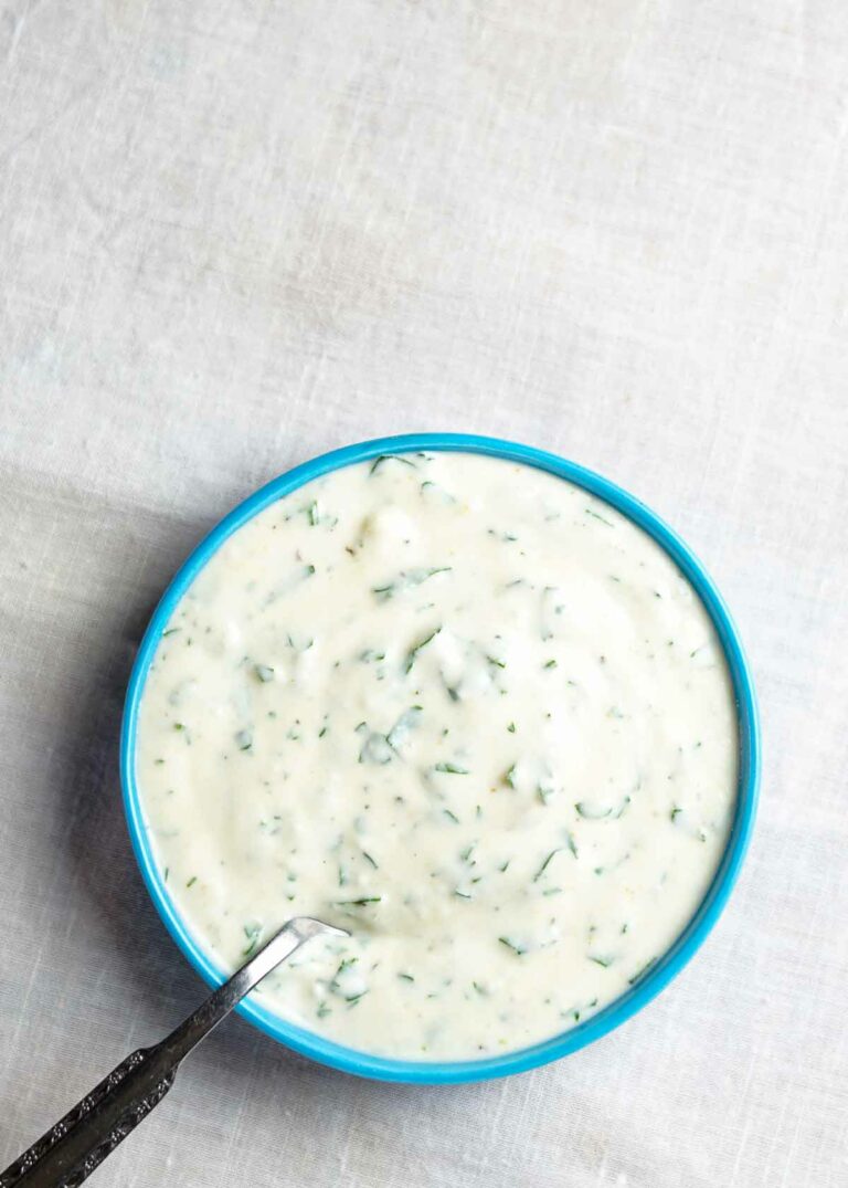 A blue bowl filled with buttermilk ranch dressing with a spoon resting in it.