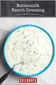 A blue bowl filled with buttermilk ranch dressing with a spoon resting in it.