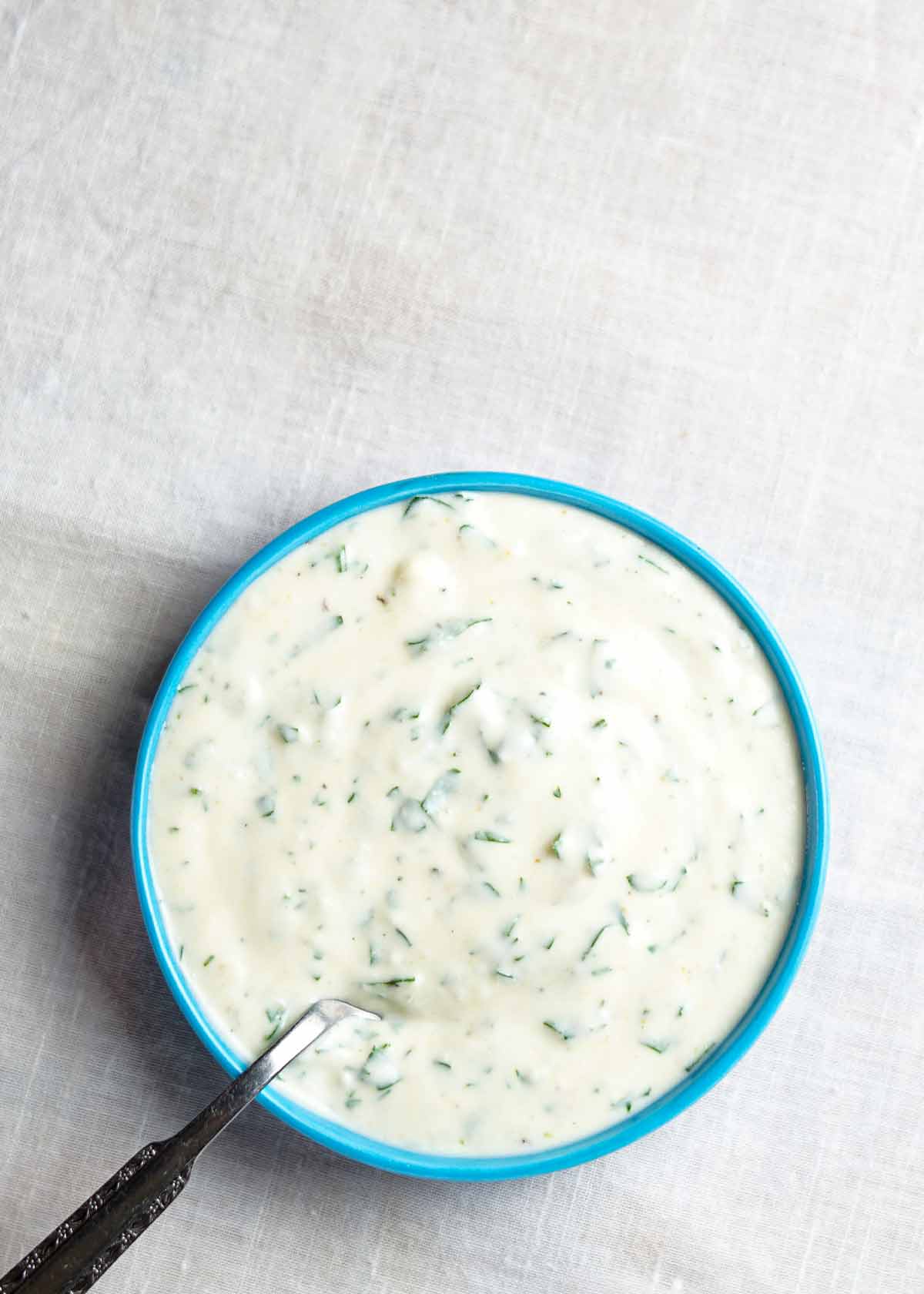 A blue bowl filled with buttermilk ranch dressing with a spoon resting in it.