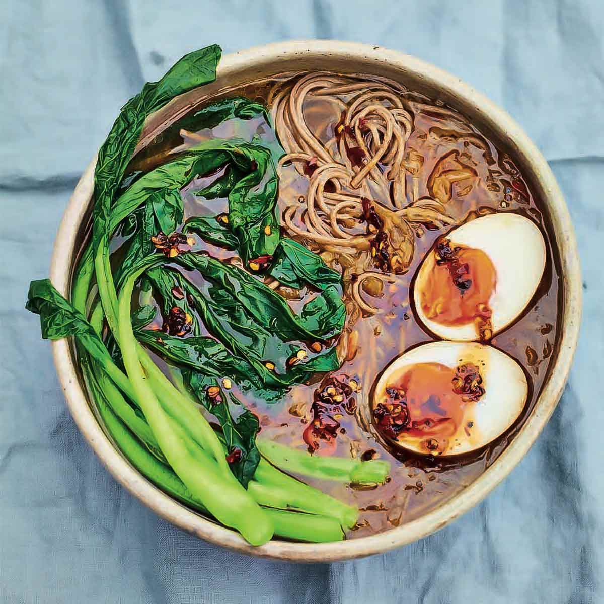 A bowl of caramelized onion ramen with chile, choy sum, and soft boiled egg.