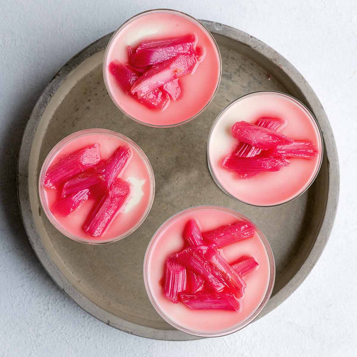 Four individual servings of cardamom panna cotta with rhubarb on a serving tray.