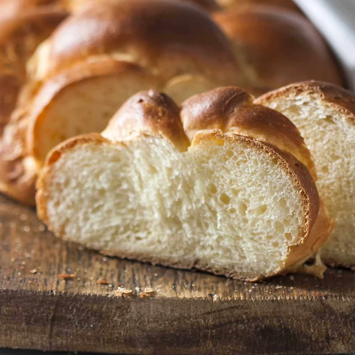 A partially sliced loaf of challah on a wooden cutting board.