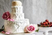 A cheese "wedding" cake made with four rounds of cheese, fresh roses, and bowls of roasted grapes and marshmallows on the side.