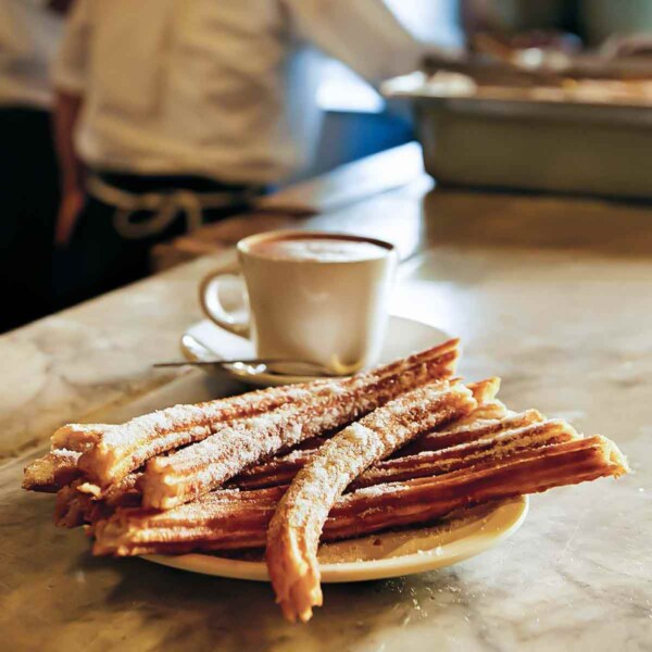 A plate of churros with a cup of hot chocolate in the background