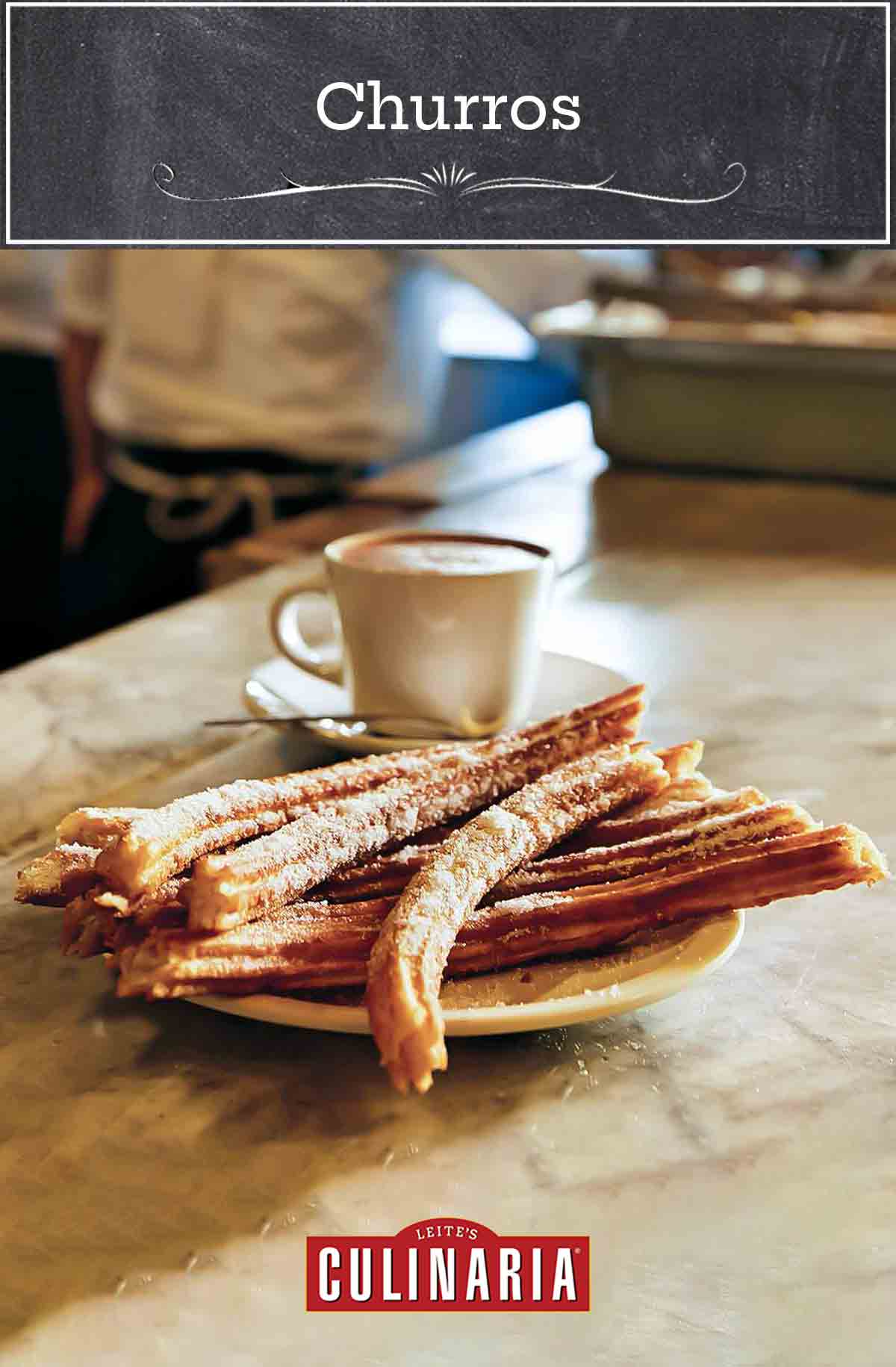 A plate of churros with a cup of hot chocolate in the background