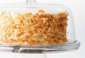 A whole coconut carrot cake, covered in toasted coconut on a glass cake stand, covered with a glass dome.
