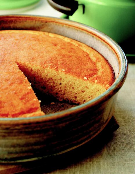 A cake pan of golden brown cornbread with a slice removed