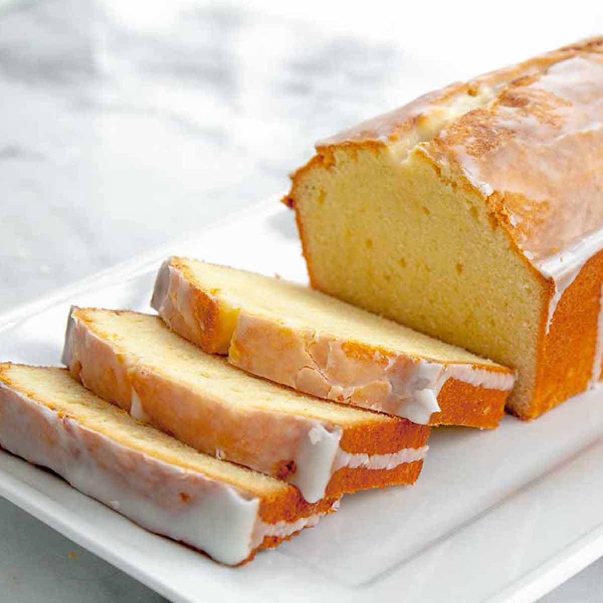A partially sliced loaf of cream cheese pound cake with lemon glaze.