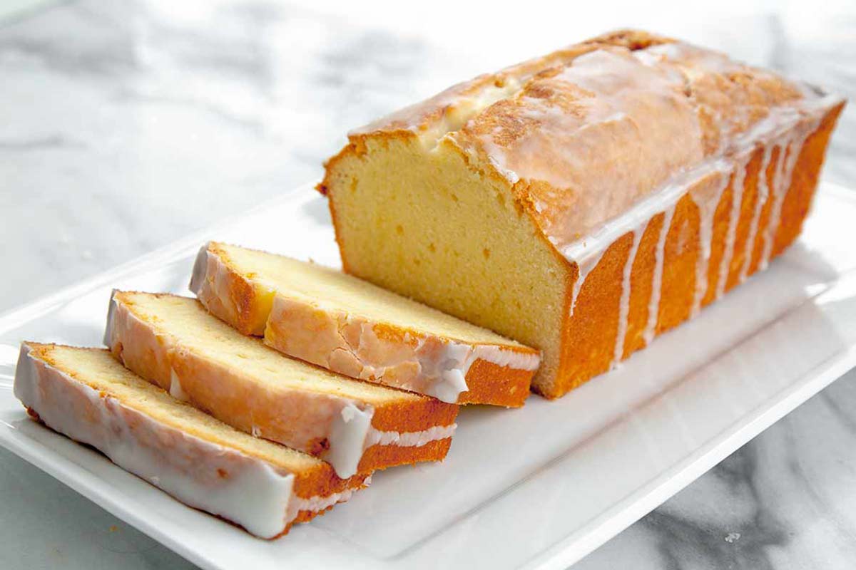 A partially sliced loaf of cream cheese pound cake with lemon glaze.