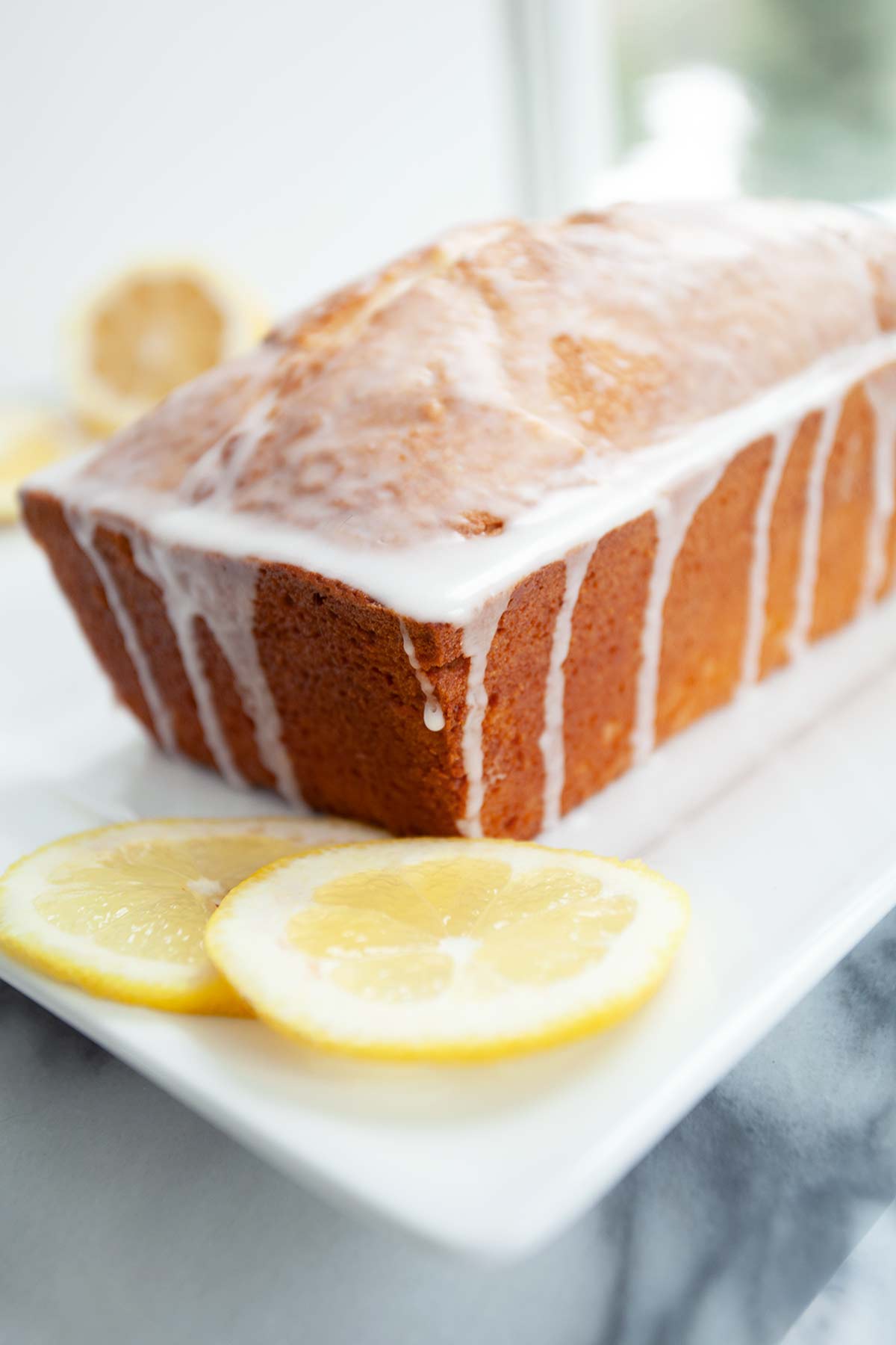 A partially sliced loaf of cream cheese pound cake with lemon glaze.