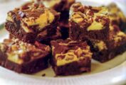 Plate of cream cheese swirl brownies with layers of chocolate, cheese cake, Heath bar, and pecans