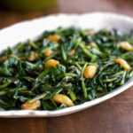 A white oval dish filled with dandelion greens sautéed in duck fat on a wooden table.