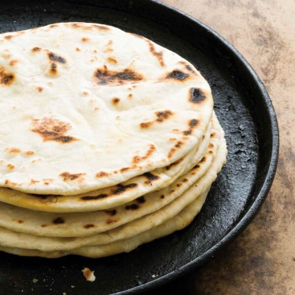 A stack of flour tortillas with bacon fat on a cast-iron skillet.