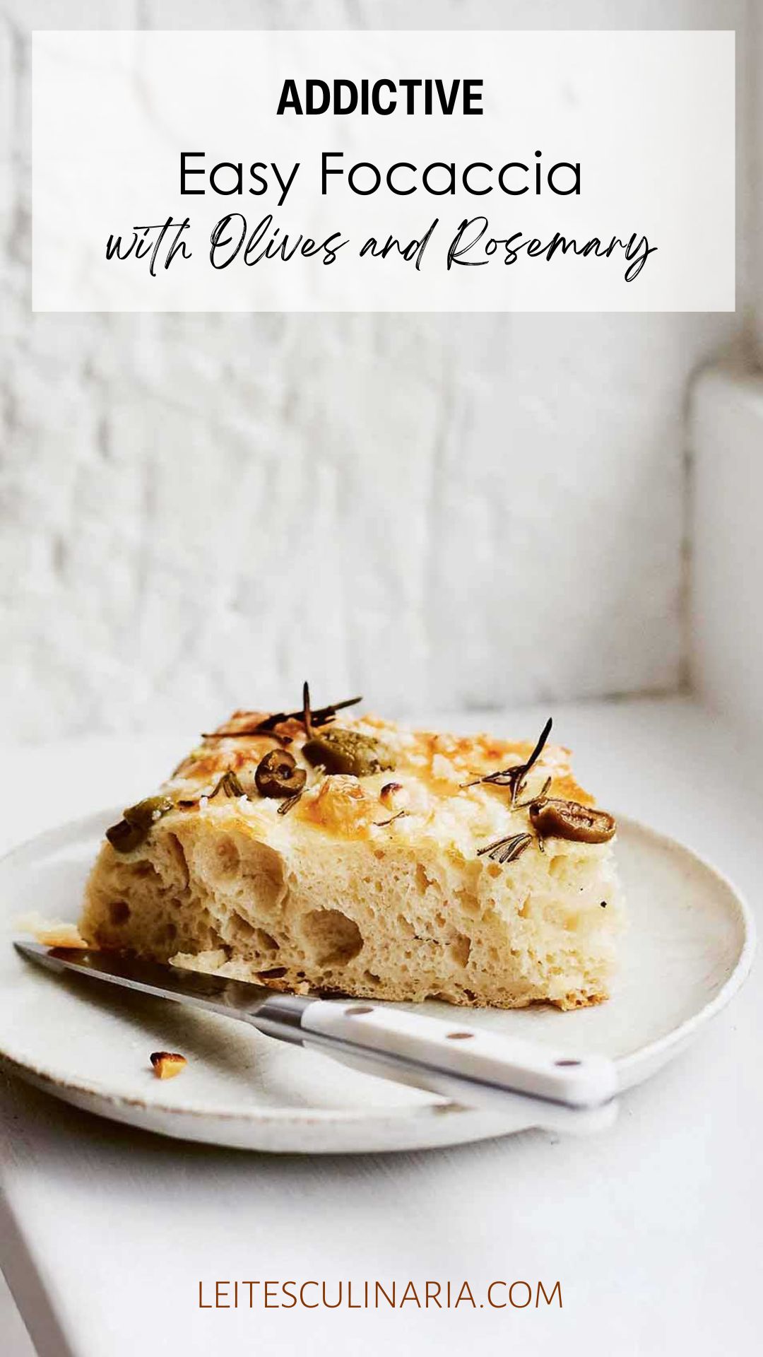 A slice of focaccia with olives and rosemary on a white plate with a knife resting beside it.