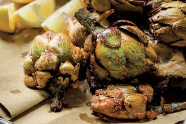 A platter of fried artichokes on paper with lemon wedges.