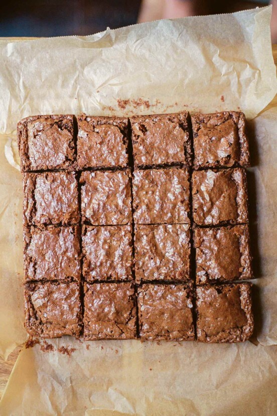 A batch of gluten-free brownies with soy sauce or tamari cut into 16 squares on a piece of parchment.