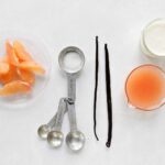 The components of grapefruit and vanilla bean panna cotta -- cream, grapefruit juice and segments, sugar, and two vanilla beans -- arranged on a white surface.